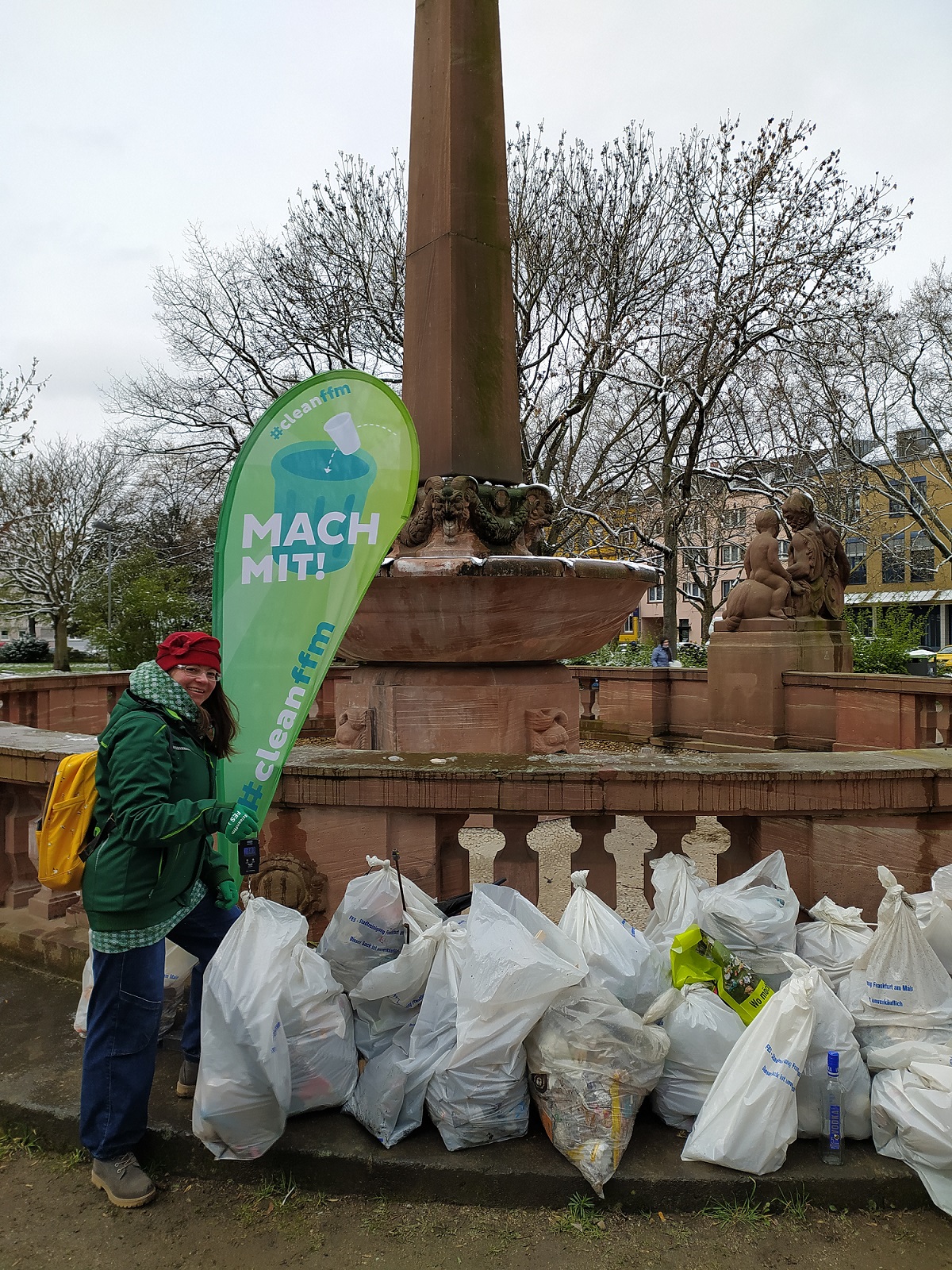 Foto: Viele gefüllte Müllsäcke, daneben steht eine Frau vor einer Beachflag mit Text „MACH MIT!“